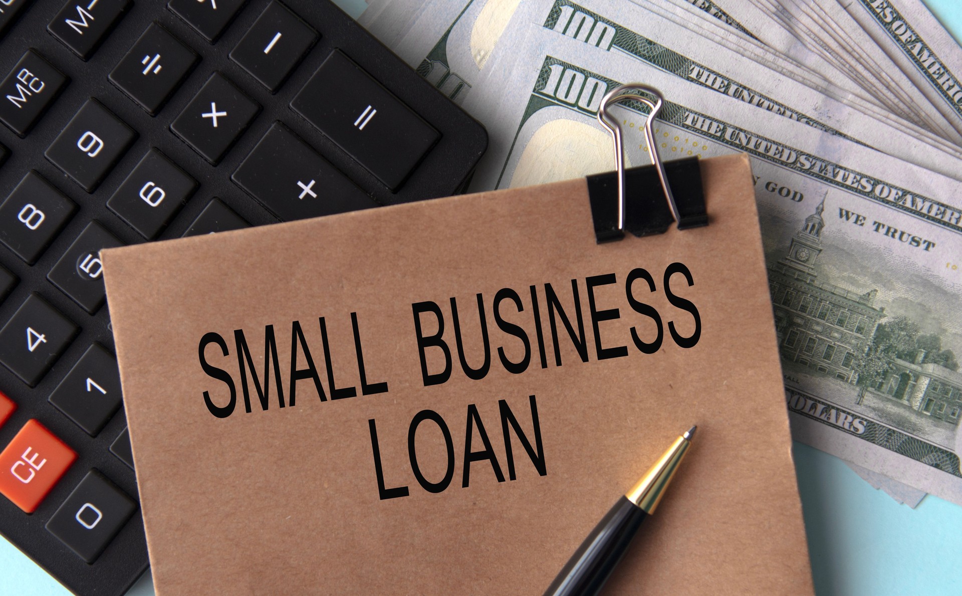 SMALL BUSINESS LOAN- words on brown paper on the background of calculator and banknotes